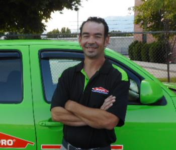 a man in a black shirt standing in front of a green SERVPRO truck