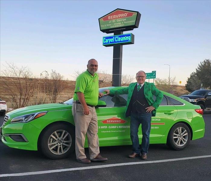 Two men standing in front of a SERVPRO car. 